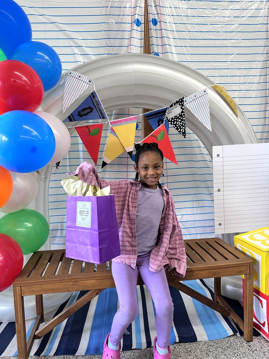 Crowned & Ready 2026: A child seated with a purple take-home gift bag