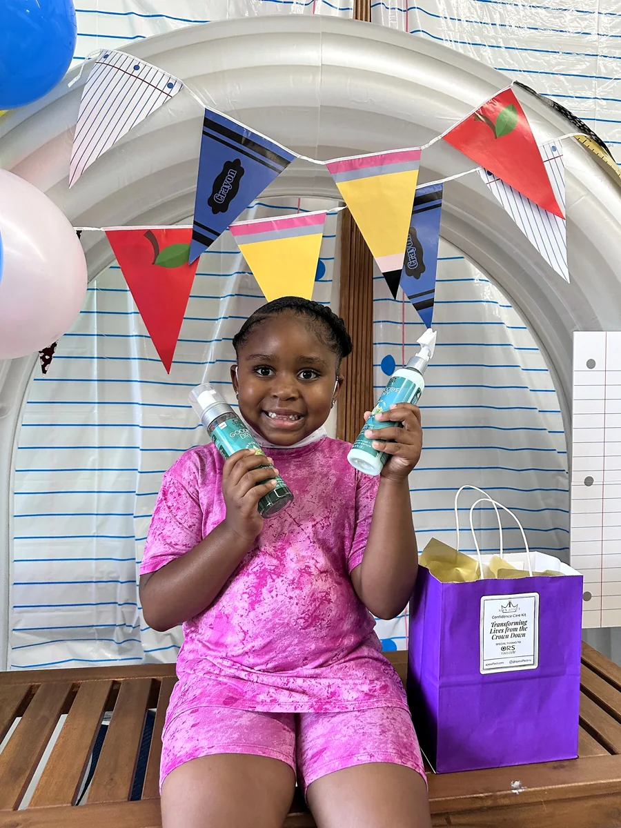 Crowned & Ready 2026: A smiling child holding haircare products beside a gift bag