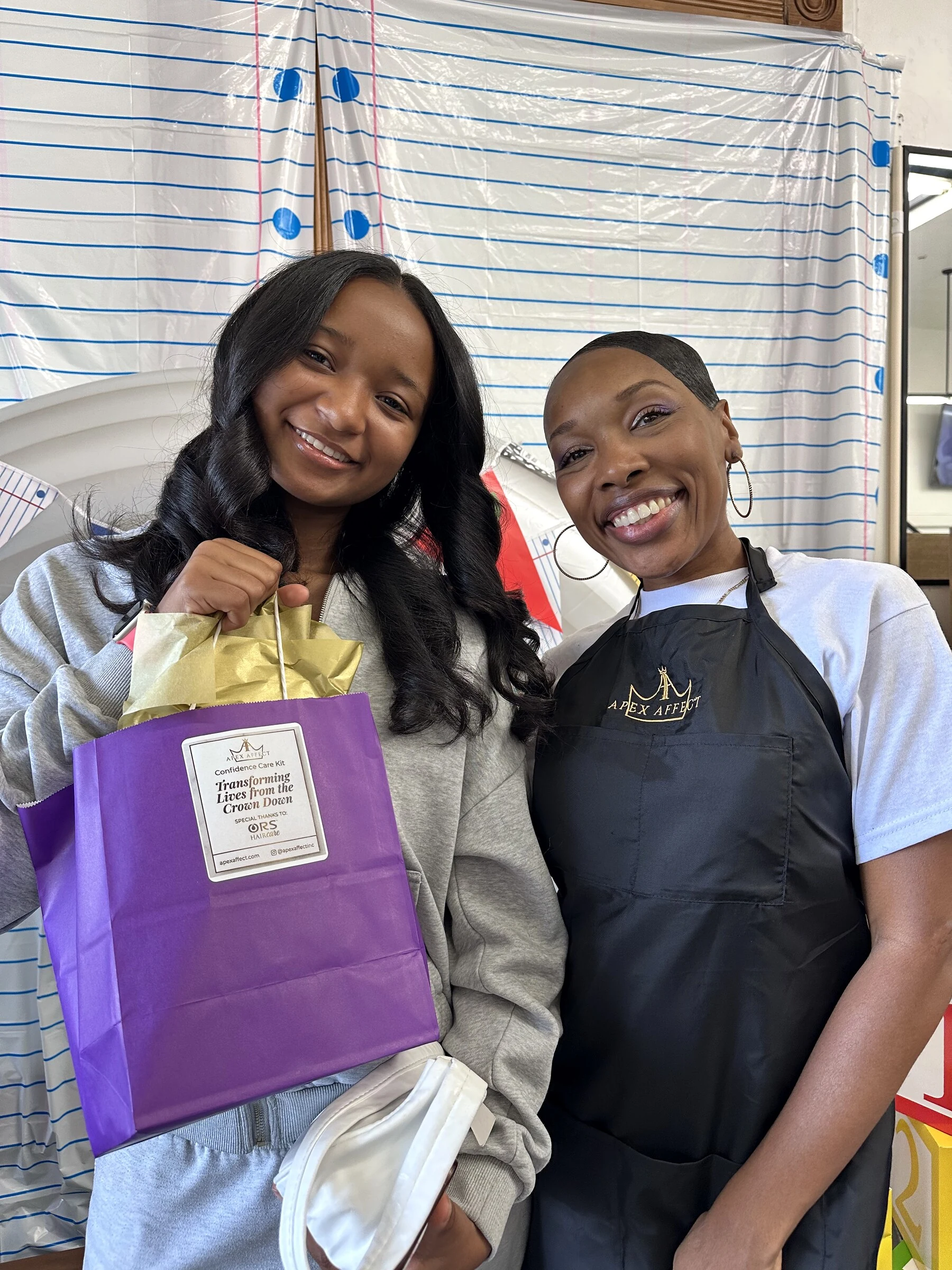 Crowned & Ready 2026: Two smiling participants sharing a purple take-home gift bag in the salon